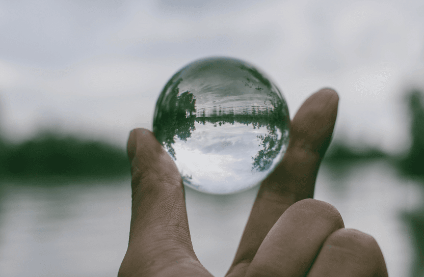 Hand holding a transparant ball, with the view of a forest and a lake in it.