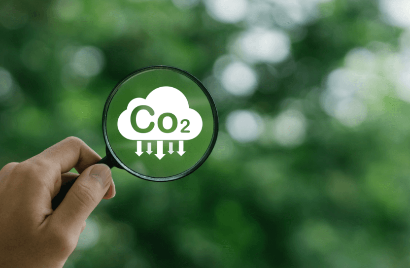 En hand håller i ett förstoringsglas riktat mot en illustation av ett moln med texten co2.
