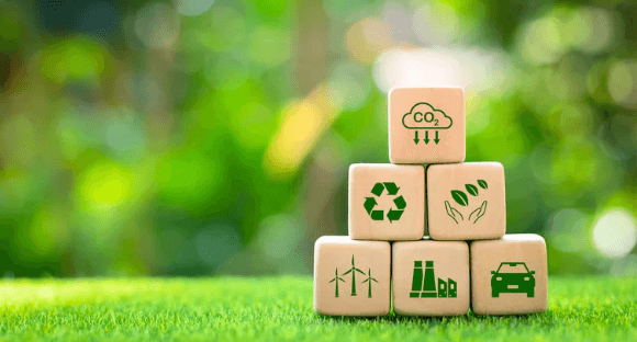 Cubes with sustainability symbols are stapeled on a lawn.